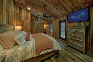A rustic bedroom with a bed, a ceiling fan, a television, and wooden walls. - A View From Above | Private Pool | Hot Tub | Mountain Views (Sevierville)