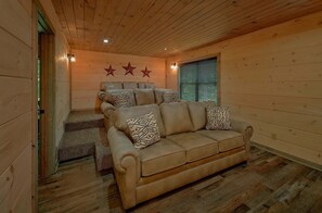 Ein gemütliches Cabin-Interieur mit einer Sofagarnitur, Holzwänden und einem Fenster mit Jalousien.