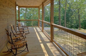 Een houten terras met schommelstoelen, een leuning en uitzicht op een bos.