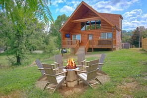 A wooden cabin with a deck, a fire pit with chairs, and a clear sky. - A Beary Good Life | Hot Tub | Close to Tanger Outlets | Minutes from the Parkway (Sevierville)