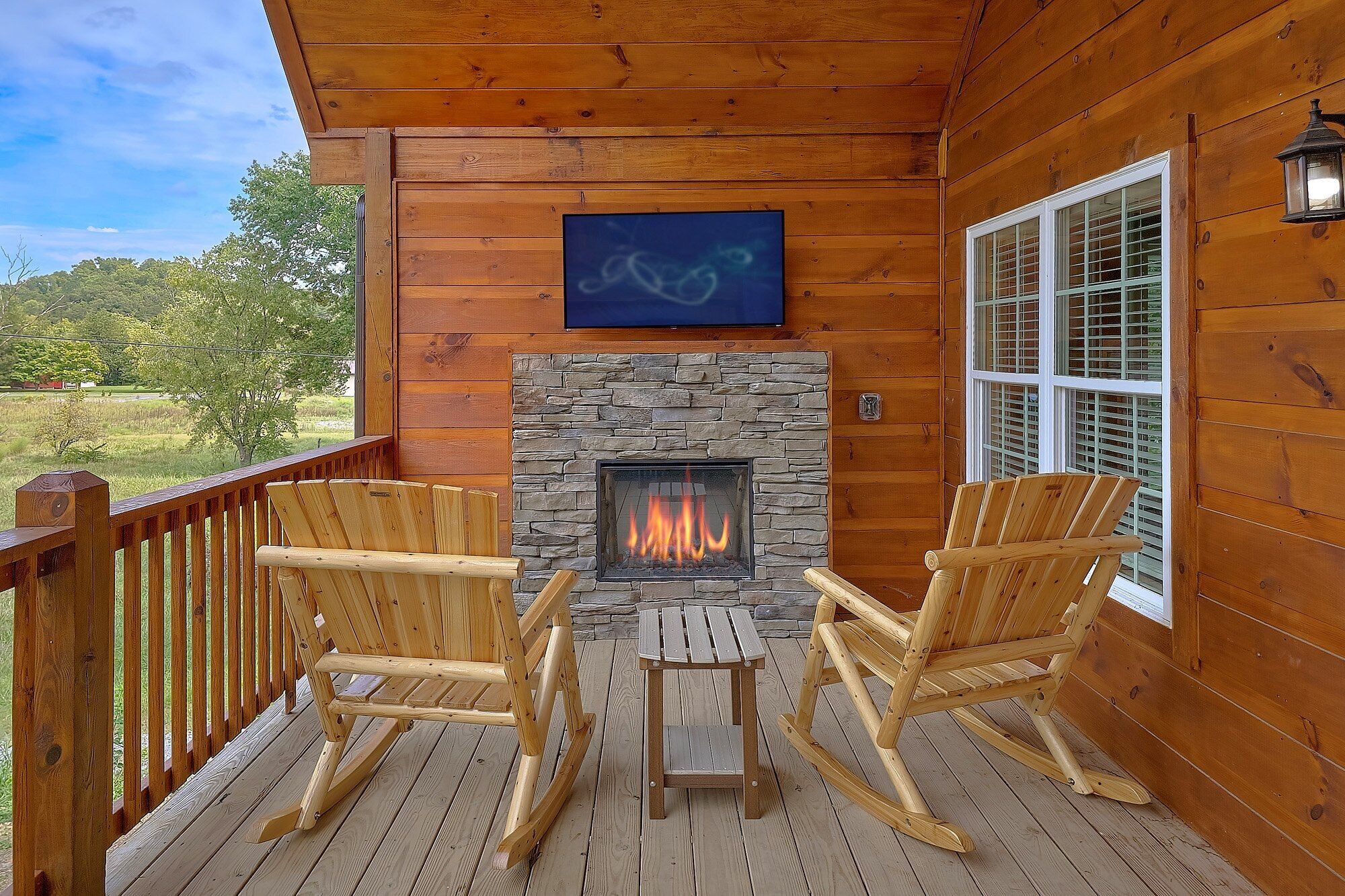 A wooden deck with a stone fireplace, two rocking chairs, and a television mounted above the fireplace.