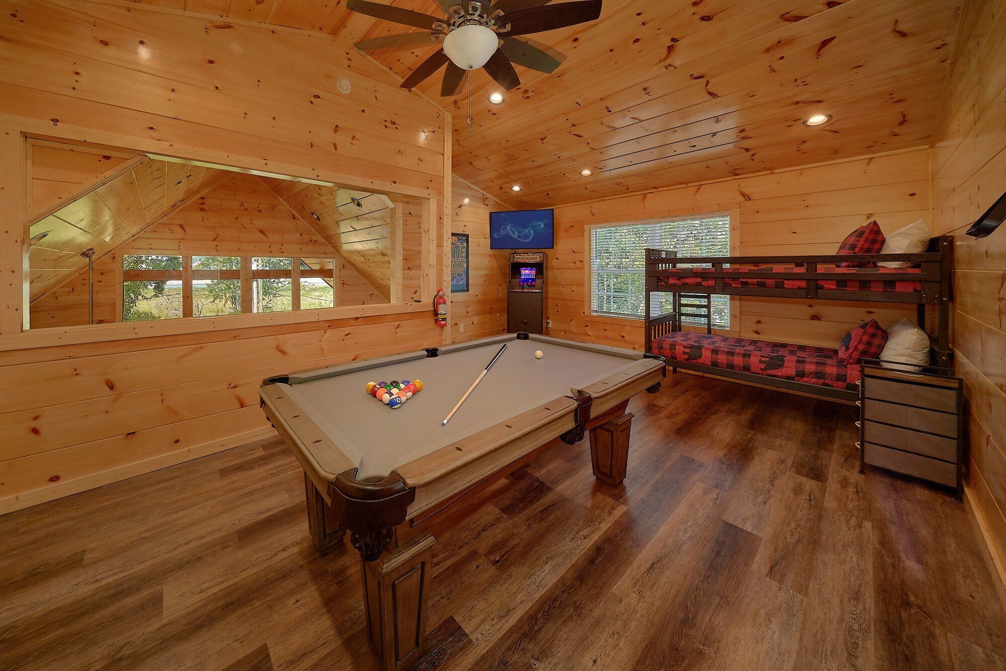 Un intérieur en bois avec une table de billard, des lits superposés et un ventilateur de plafond.