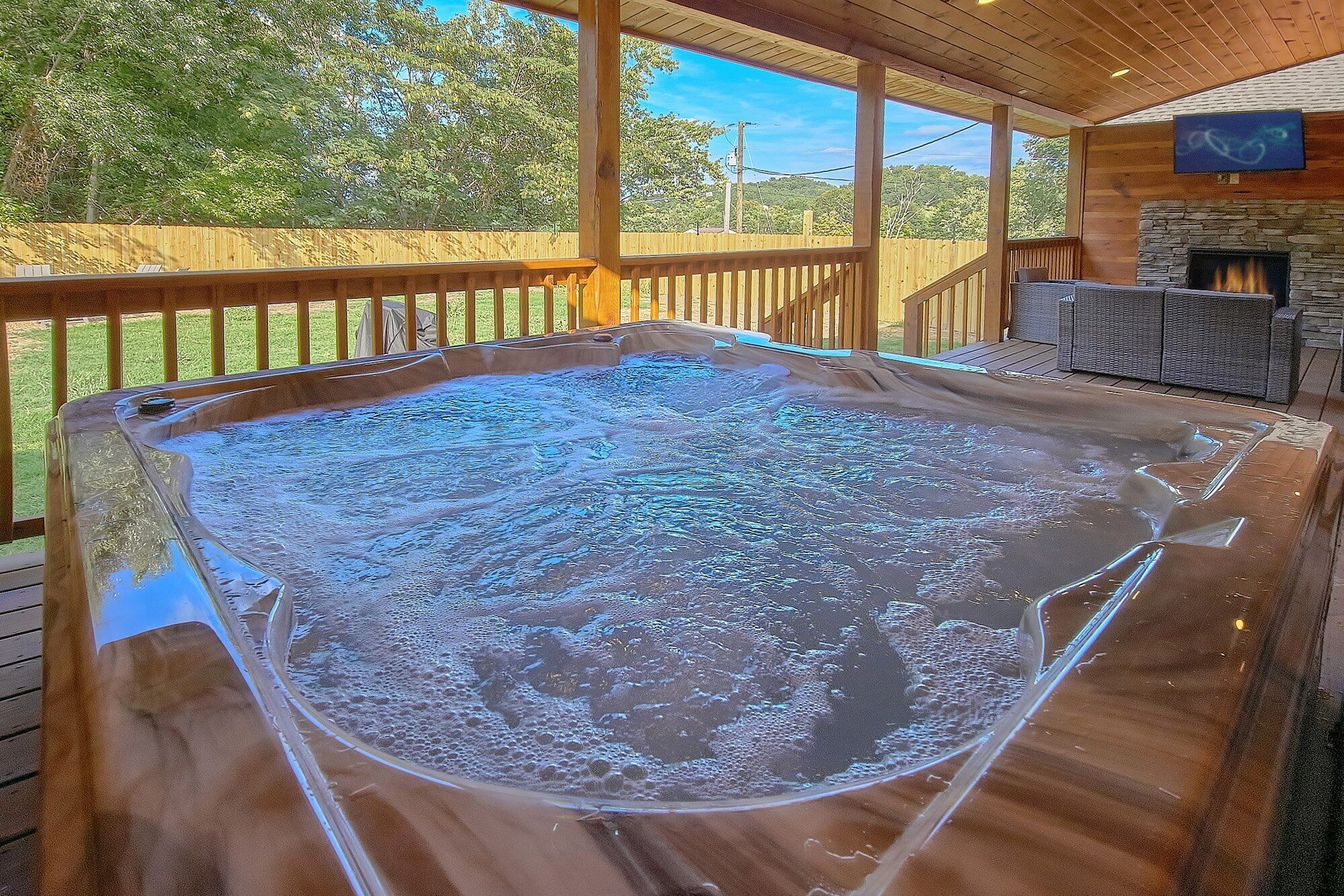 Ein Whirlpool auf einer Holzterrasse mit Kamin aus Stein und Gartenmöbeln.