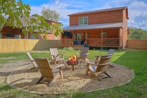 A wooden cabin with a deck, surrounded by a fire pit with chairs. - Makin' Memories | Hot Tub, Game Room, Fire Pit, Fireplace + Free Attraction Tickets (Sevierville)