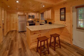 A cabin-style kitchen with wooden walls, a granite countertop, and a refrigerator. - Makin' Memories | Hot Tub, Game Room, Fire Pit, Fireplace + Free Attraction Tickets (Sevierville)
