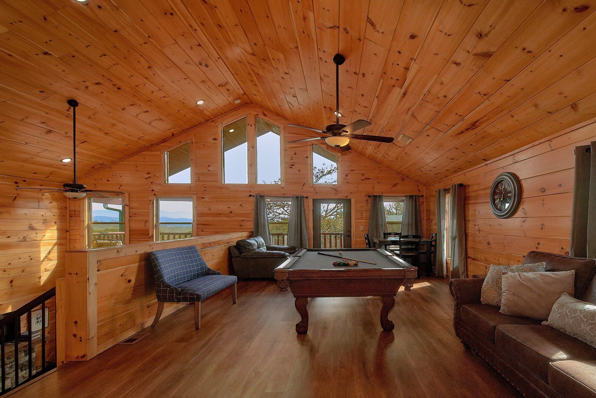 A wooden interior with a pool table, seating area, and large windows.