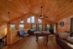 Ein Holzinterieur mit Billardtisch, Sitzgelegenheit und großen Fenstern.