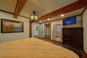 A bedroom with a large bed, wooden beams, a ceiling light, a TV, and a wardrobe. - Jewell's Place | Fire Pit, Pet Friendly, Fireplace + Free Attraction Tickets (Sevierville)
