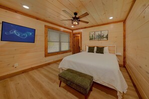 A bedroom with a bed, a bench, a ceiling fan, a window with blinds, and a painting on the wall. - Smoky Mountain Getaway | Private Pool, Theater, Smoky Mtn Views, Hot Tub + Free Attraction Tickets (Gatlinburg)