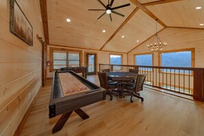 A wooden-floored room with a pool table, a dining table with chairs, and a view of the outdoors through large windows. - Smoky Mountain Getaway | Private Pool, Theater, Smoky Mtn Views, Hot Tub + Free Attraction Tickets (Gatlinburg)