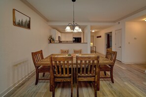A dining room with a wooden table and chairs, a hanging light fixture, and a kitchen area in the background. - Mountain View 3206 | Pigeon Forge, Resort Pool, Fireplace + Free Attraction Tickets (Pigeon Forge)