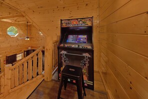 A wooden interior with a retro arcade machine, a staircase, and a small table. - Swimming in the Smokies | Indoor Pool, Hot Tub, Game Room, Sleeps 12 + Free Attraction Tickets (Pigeon Forge)