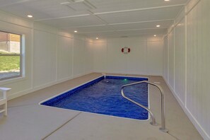A room with a blue pool, a white bench, and a fire safety sign on the wall. - Swimming in the Smokies | Indoor Pool, Hot Tub, Game Room, Sleeps 12 + Free Attraction Tickets (Pigeon Forge)