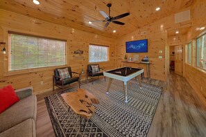 A wooden cabin interior with a ceiling fan, two windows with blinds, a billiards table, a television, and a fireplace. - Misty Shadows Splash | Private Pool, Hot Tub, Game Room, Fireplace + Free Attraction Tickets (Wears Valley)