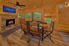 A wooden interior with a stone fireplace, a dining table with chairs, a ceiling fan, and large windows. - Misty Shadows Splash | Private Pool, Hot Tub, Game Room, Fireplace + Free Attraction Tickets (Wears Valley)