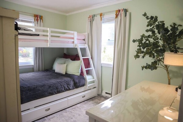 A bunk bed with a ladder, a bedside table, a lamp, and a window with curtains.
