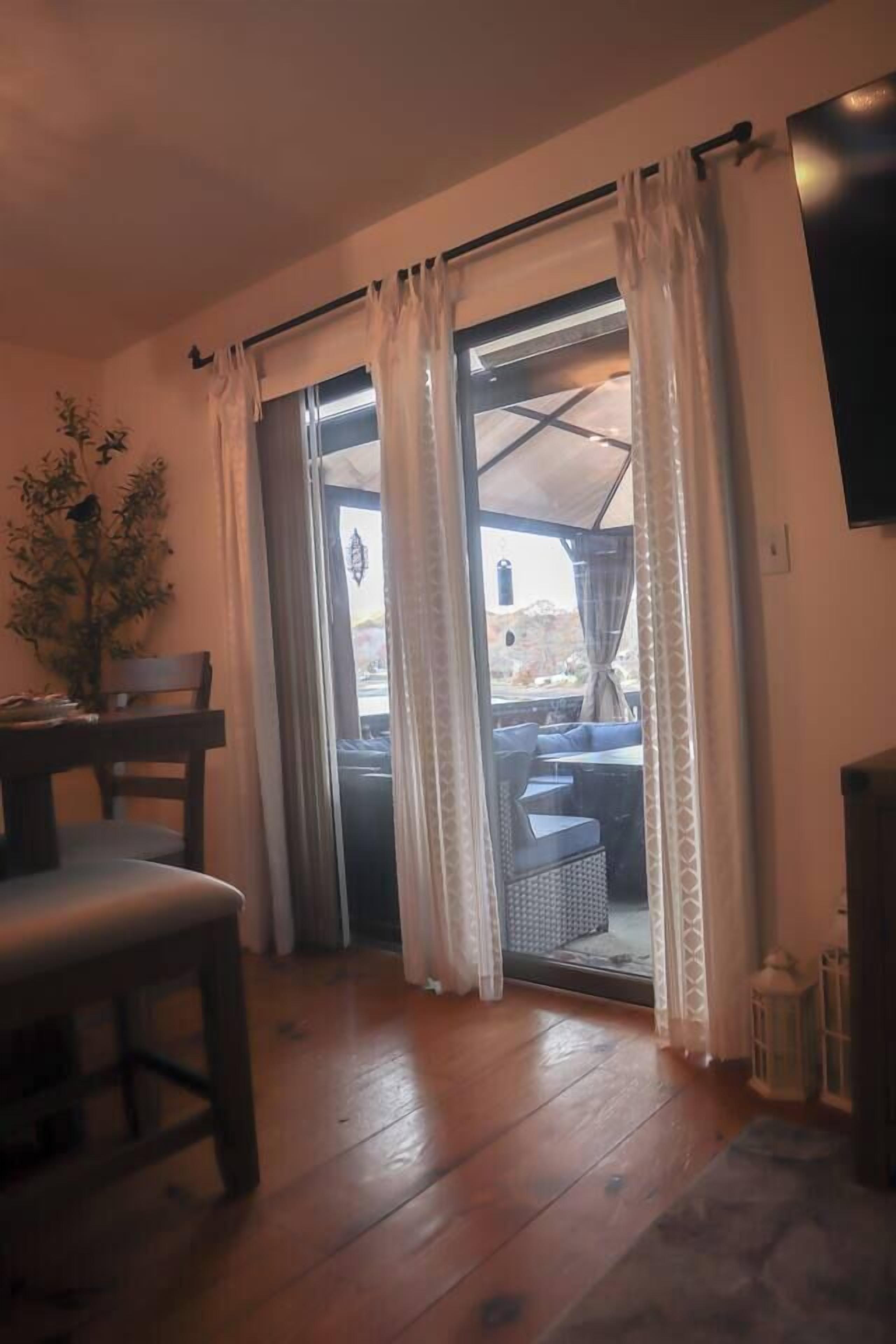 Een kamer met houten vloer, een eettafel met stoelen, een aan de muur bevestigde televisie en een glazen schuifdeur die uitkomt op een terras.