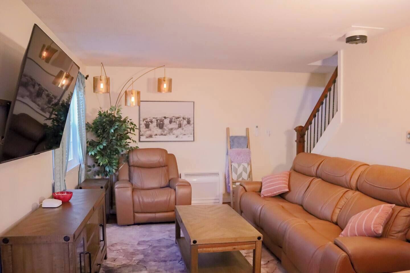 Ein Wohnzimmer mit braunem Ledersofa, einem braunen Ledersessel, einem Holztisch und einem an der Wand befestigten Fernseher.