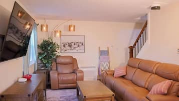 Ein Wohnzimmer mit braunem Ledersofa, einem braunen Ledersessel, einem Holztisch und einem an der Wand befestigten Fernseher.