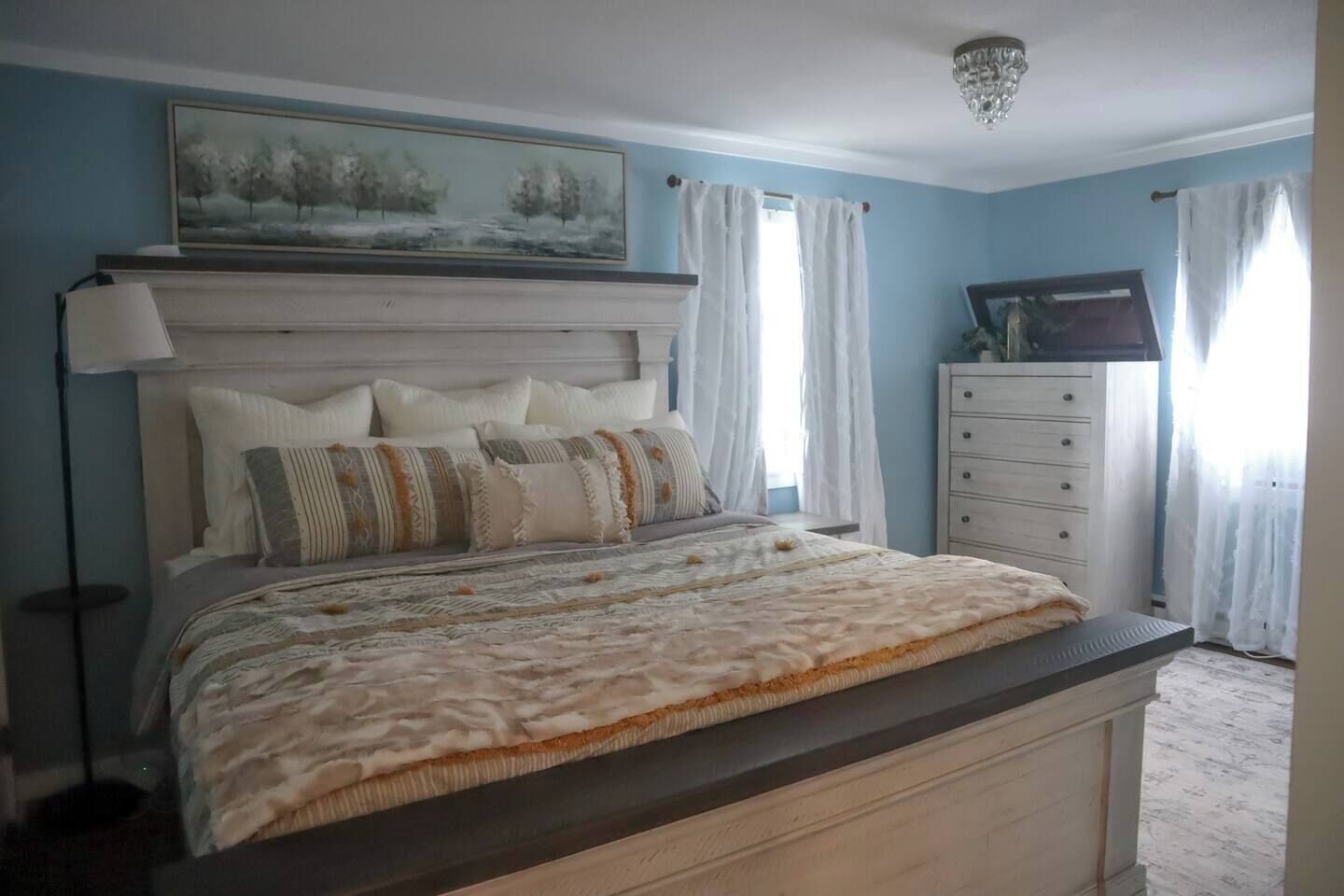 Een slaapkamer met een bed, een dressoir, een nachtkastje, een schilderij en een kroonluchter.