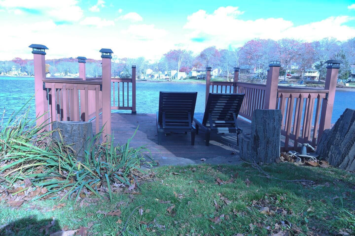 A dock with two chairs facing a body of water, surrounded by a wooden fence and vegetation.