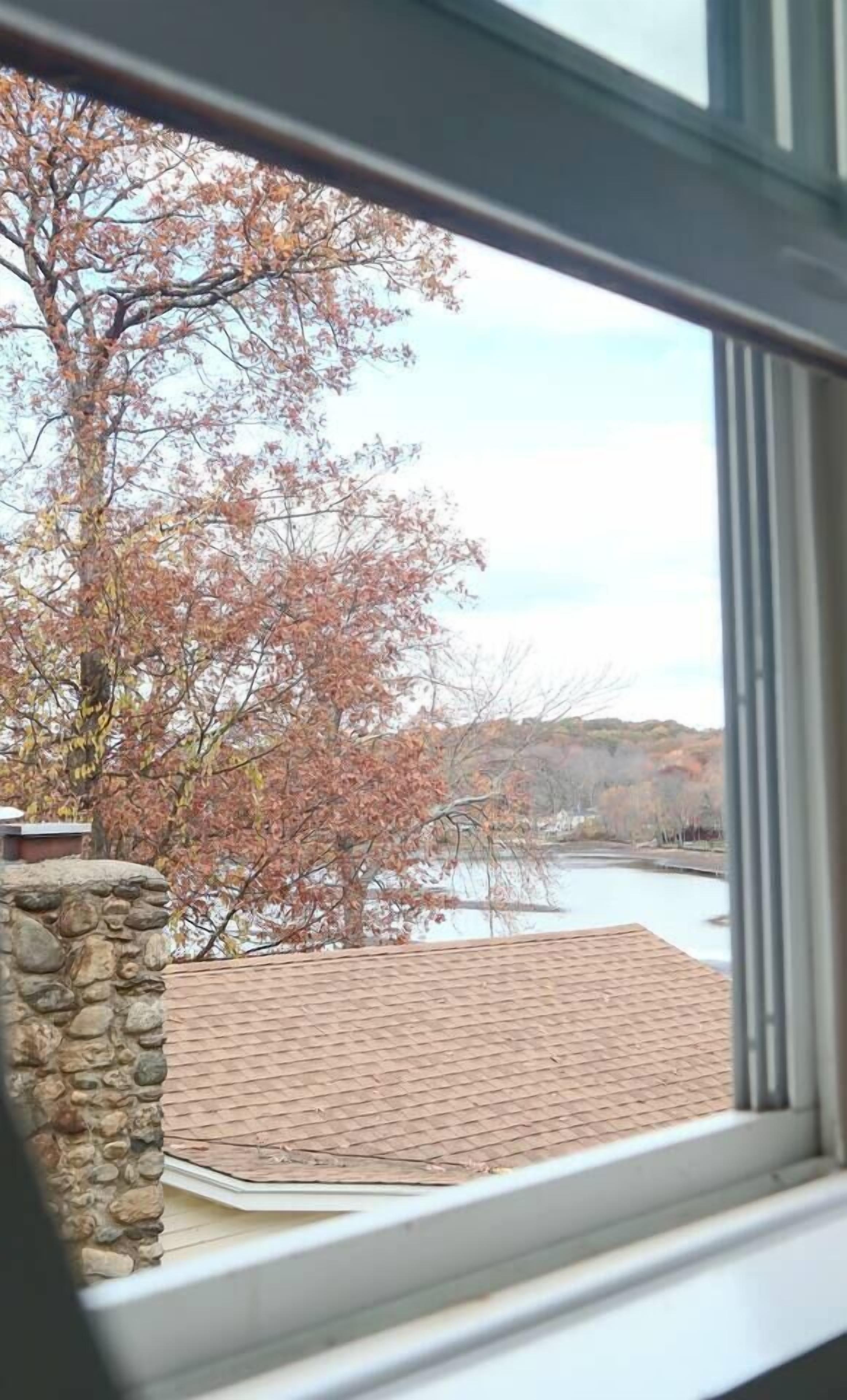 A view through a window of a stone pillar, a brick roof, and a river with trees in the background.