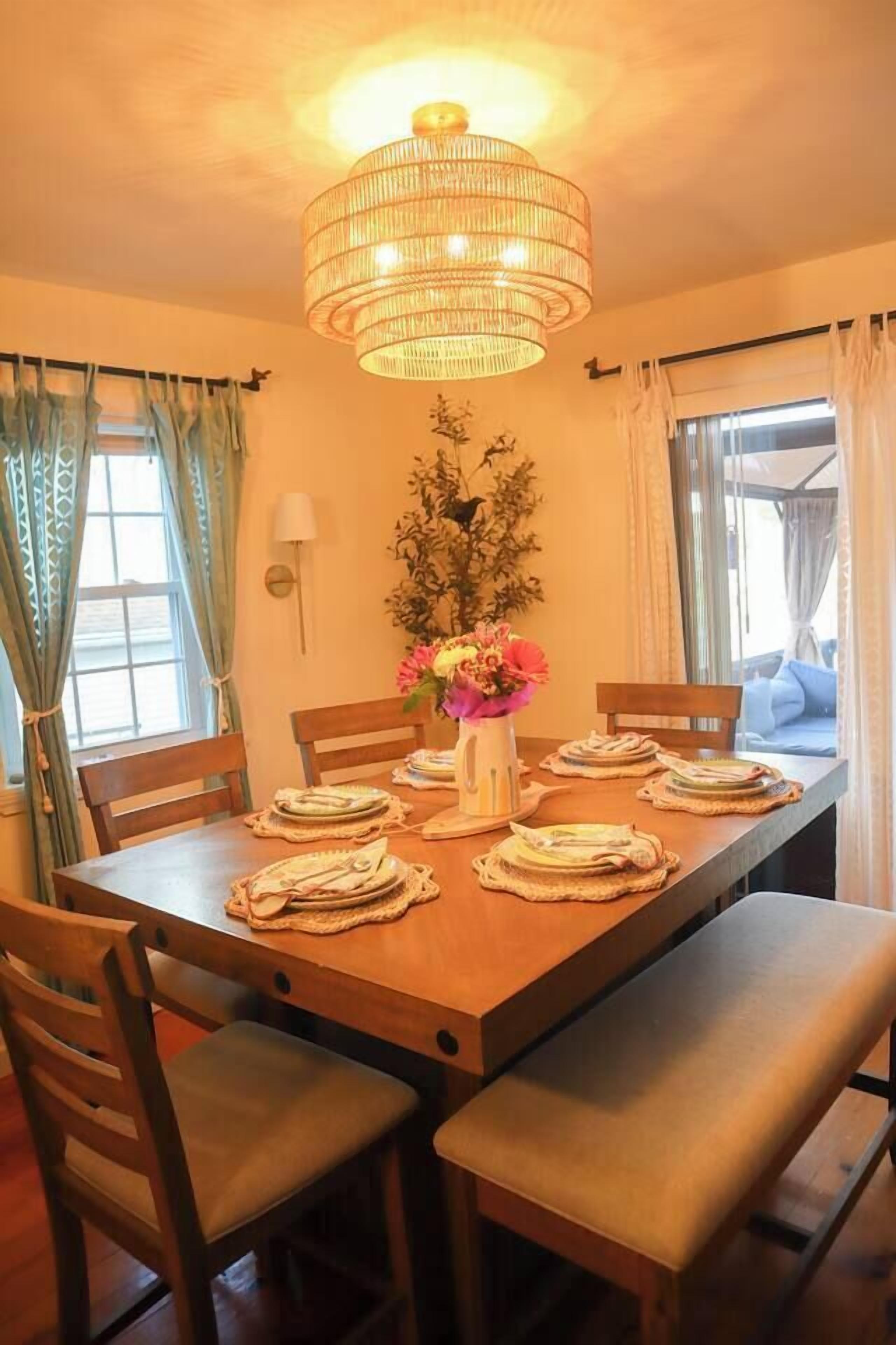 A dining area with a wooden table set for four, a decorative vase with flowers, and a hanging light fixture.
