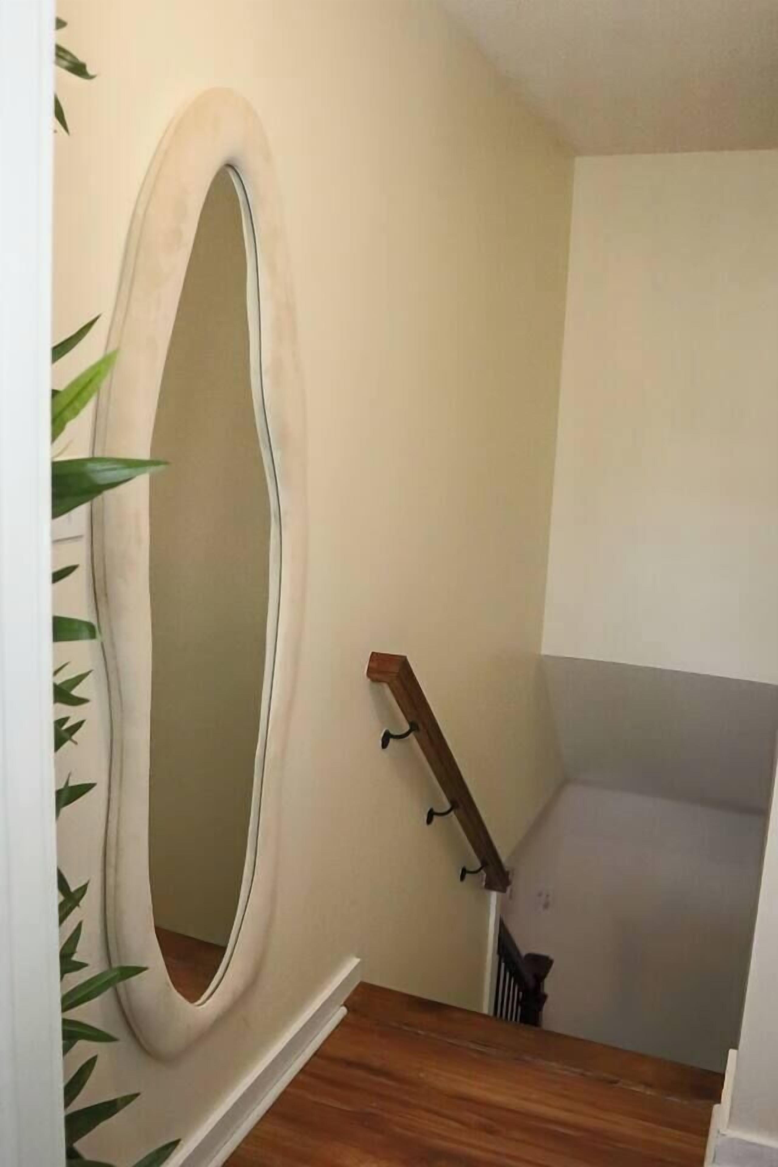A staircase with a wooden handrail and a white wall with a large, oval-shaped mirror.
