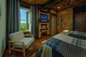 A cozy room with a bed, a chair, a fireplace, and a television. - KB Lodge Cabin Rental (Gatlinburg)