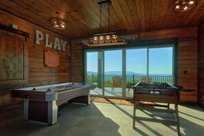 Ein Holzinterieur mit einem Kicker, einem Billardtisch und einer Bar mit Blick ins Freie.