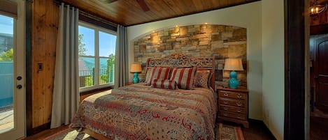 Un dormitorio con una cama grande, una pared de piedra, un ventilador de techo y vistas a través de una ventana.
