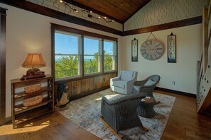 A room with a large window, wicker furniture, a lamp, and a wall clock. - KB Lodge Cabin Rental (Gatlinburg)