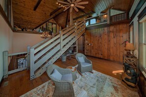 A spacious interior with a wooden staircase, wicker furniture, and a large window. - KB Lodge Cabin Rental (Gatlinburg)