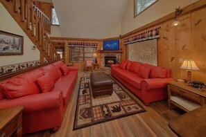 A cozy living room with red sofas, a fireplace, and a television. - Bear Creek Ridge Cabin Rental (Wears Valley)