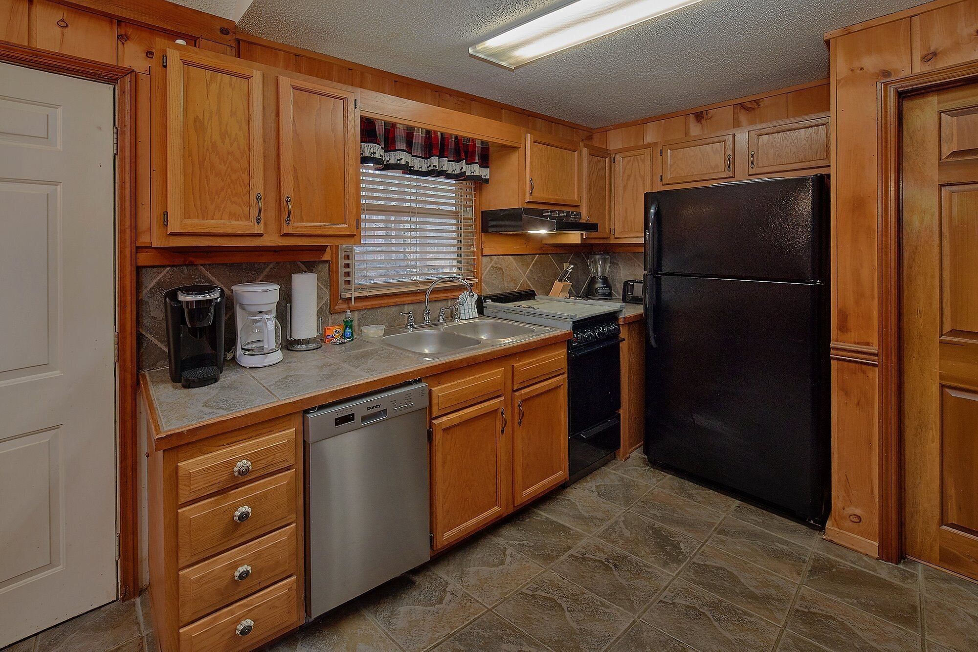 A kitchen with wooden cabinets, a black refrigerator, a dishwasher, and a coffee maker.