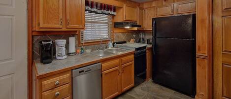 A kitchen with wooden cabinets, a black refrigerator, a dishwasher, and a coffee maker.