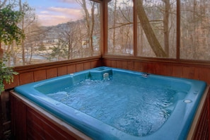 A hot tub with a wooden exterior and a view of a snowy landscape through large windows. - Bear Creek Ridge Cabin Rental (Wears Valley)