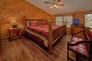 A wooden cabin bedroom with a bed, a nightstand, a chair, a desk, and a ceiling fan. - Bear Creek Ridge Cabin Rental (Wears Valley)
