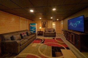 A cozy living room with a leather couch, a television, and a wooden wall. - The Oasis | Sleeps 28, Private Pool, Theater, Mtn Views, Hot Tub, Fire Pit + Free Attraction Tickets (Sevierville)