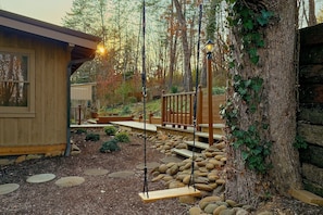 A wooden deck with a swing set, surrounded by a garden with rocks and a wooden fence. - Tucked Away | Theater, Hot Tub, Arcade, Fire Pit + Free Attraction Tickets (Wears Valley)