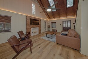 Un vaste salon doté d’une cheminée, de parquet et d’un plafond haut avec des poutres apparentes.