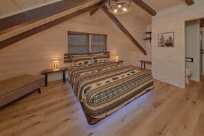 Une chambre confortable avec un plafond en pente, un grand lit avec une literie à motifs, deux lampes de chevet et une fenêtre avec des stores.