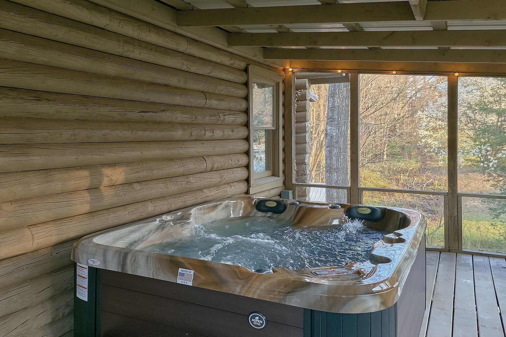 A hot tub in a log cabin with a window view of trees.