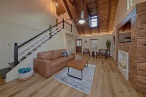 A spacious living room with a wooden staircase, a fireplace, and a ceiling fan. - Tucked Away | Theater, Hot Tub, Arcade, Fire Pit + Free Attraction Tickets (Wears Valley)