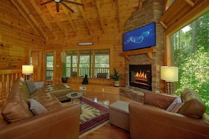 A log cabin interior with a fireplace, leather sofas, and a television mounted on the wall. - Hidden Escape | Hot Tub, Game Room, Fire Pit, Resort Pool, Fireplace + Free Attraction Tickets (Sevierville)