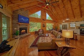 A spacious living room with a fireplace, leather sofa, and a television mounted on the wall. - Hidden Escape | Hot Tub, Game Room, Fire Pit, Resort Pool, Fireplace + Free Attraction Tickets (Sevierville)