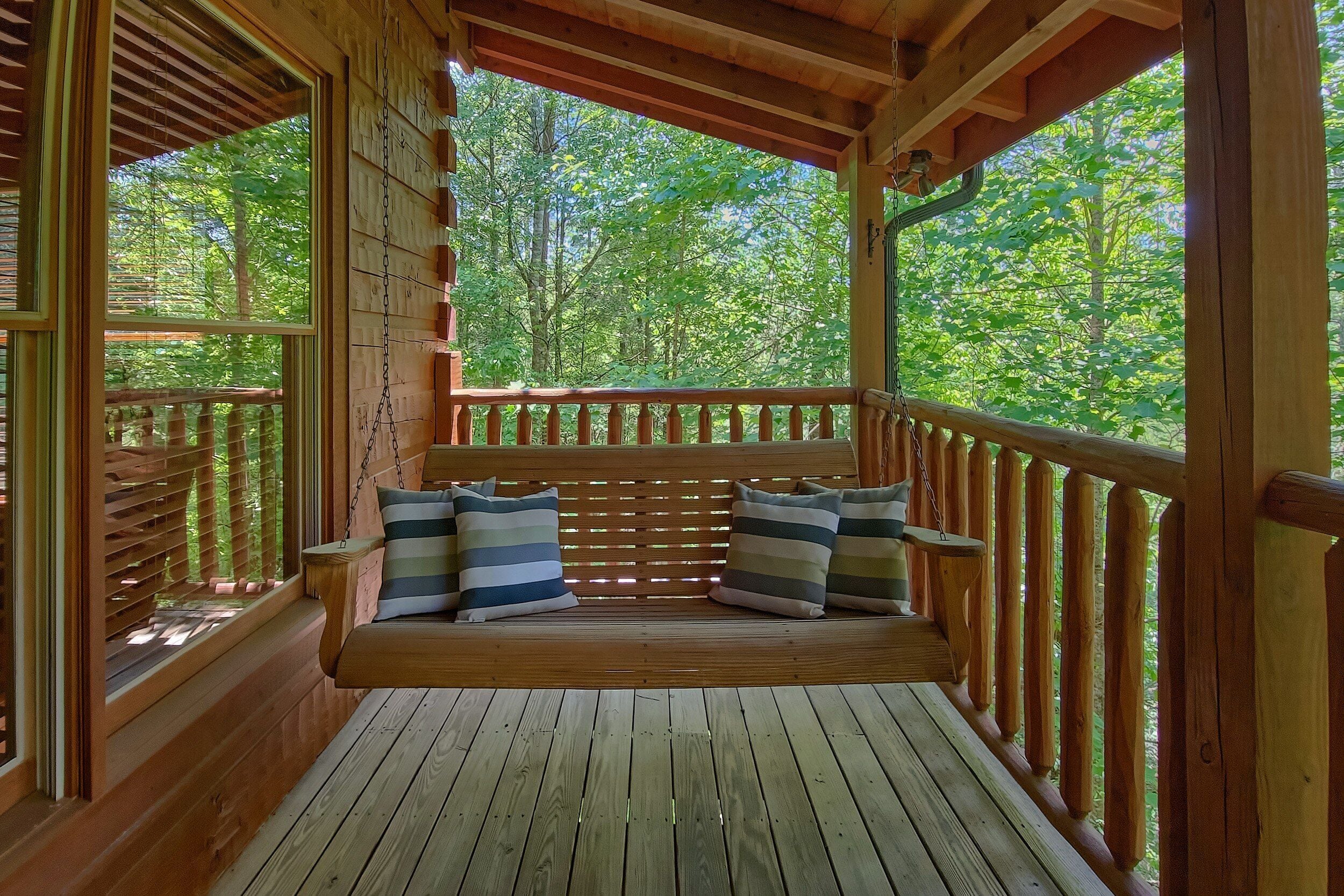 A wooden deck with a bench and pillows, surrounded by a wooden railing, overlooking a forest.