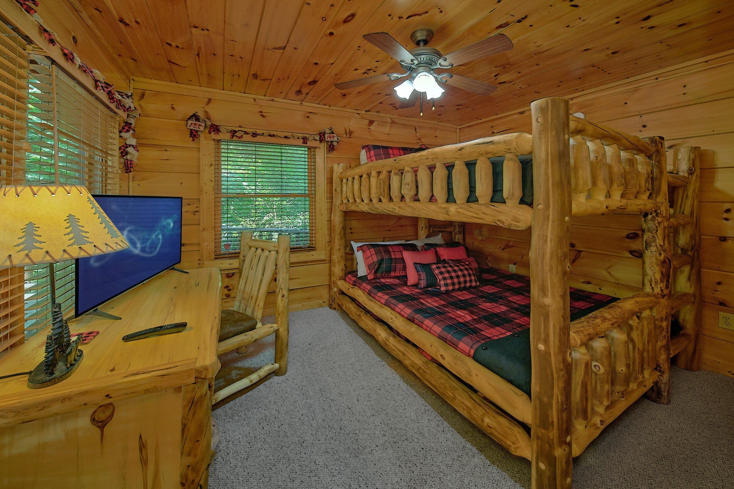 A cabin-style room with a bunk bed, a desk with a computer, a chair, and a ceiling fan.