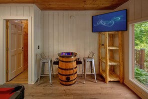 A room with a wooden barrel, two bar stools, a television mounted on the wall, and a door leading to another room. - Hidden Escape | Hot Tub, Game Room, Fire Pit, Resort Pool, Fireplace + Free Attraction Tickets (Sevierville)