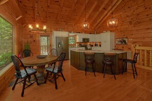 A wooden cabin interior with a dining table, chairs, a kitchen area, and a bar. - Hidden Escape | Hot Tub, Game Room, Fire Pit, Resort Pool, Fireplace + Free Attraction Tickets (Sevierville)
